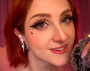 Mewlies ASMR an asmr artist with red hair, showing a close up of her face and a fluffy microphone.
