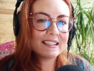 "whispers red asmr" wearing glasses with red hair and headphones.