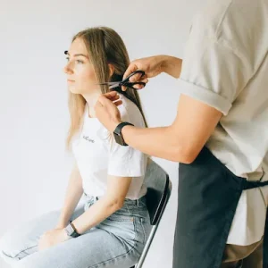 man cutting a lady's hair with black scissors the lady is wearing a white top and jeans